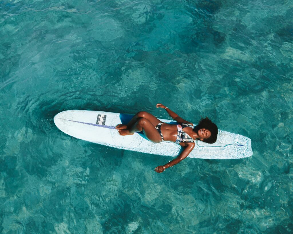A woman relaxing on a surfboard in clear blue water, smiling and enjoying a sunny day through tailored travel experiences and bookings.