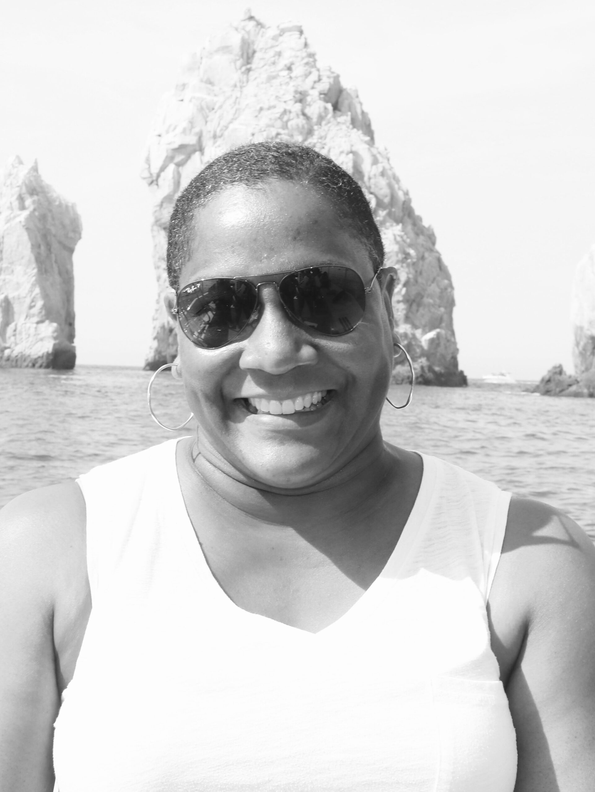 Founder woman wearing sunglasses, posing on a boat with rocky formations and calm ocean waters in the background. With Emerald Dreamscape vacations, personalized travel experiences are available. These are tailor-made for you. 